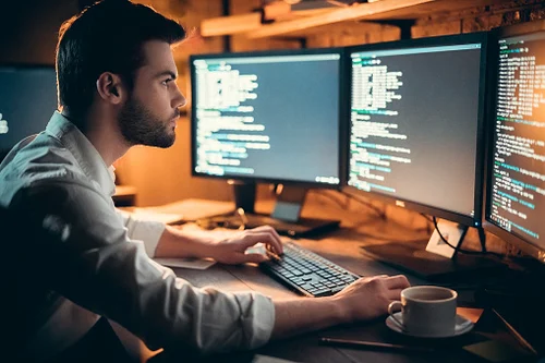 A man writes code on a computer and stares at the monitor