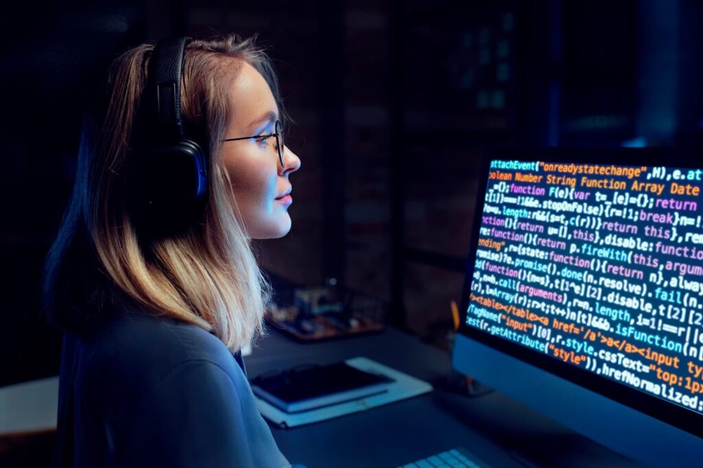 A girl in a headset sits in front of a computer screen with a code