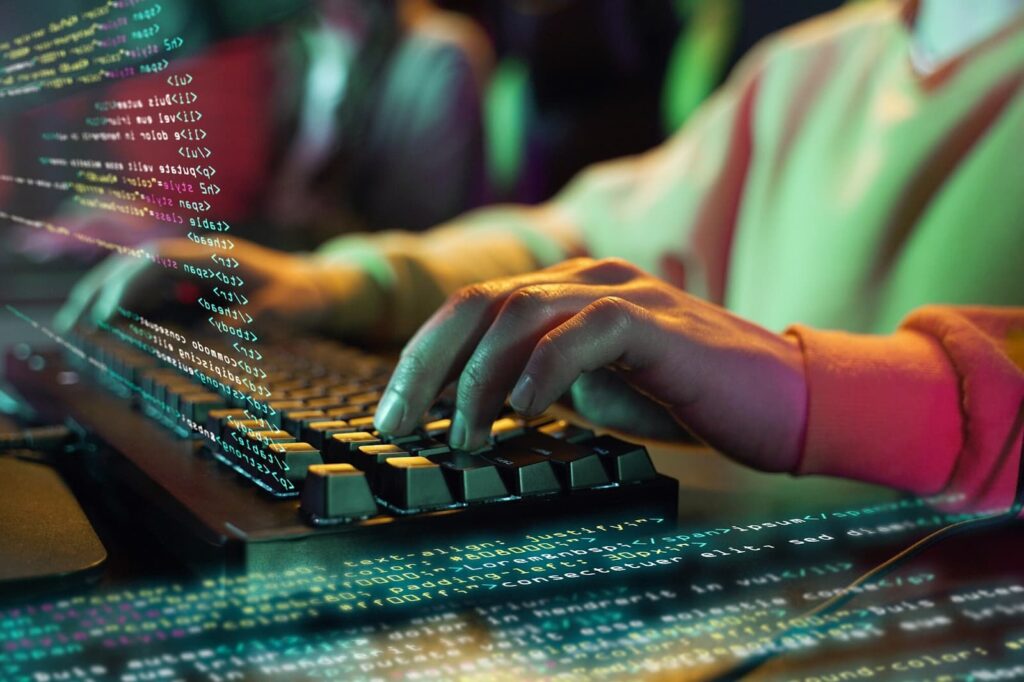 Human hands on a computer keyboard, program code in the foreground