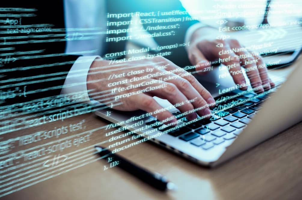A blurred image of hands typing on a laptop with code overlay