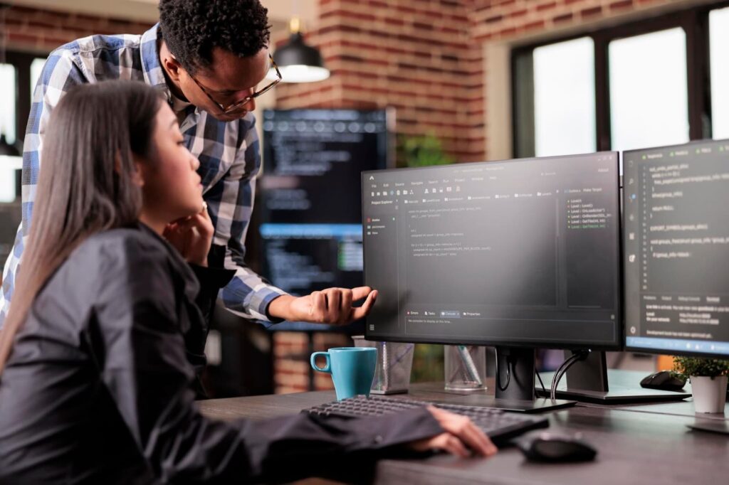 Programmers discussing code compilation while standing in front of multiple screens in a startup office